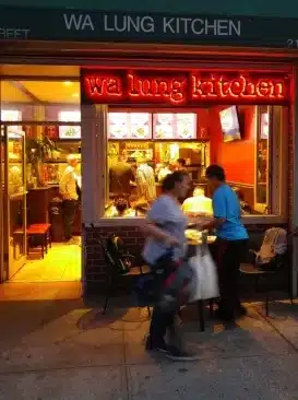 Image of the Chinese Restaurant, Wa Lung Kitchen, located in the Lower East Side of Manhattan at night with customers inside and outside the restaurant.