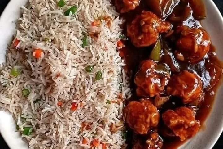 A plate of Chinese food featuring flavorful fried rice with finely chopped vegetables, served alongside Manchurian meatballs coated in a rich, dark sauce with bell peppers. The dish is beautifully presented on a white plate against a dark background.