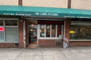 Exterior shot of Wa Lung Kitchen, a restaurant with a green awning and brick facade, located on Grand Street.